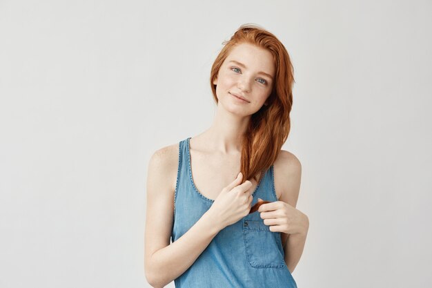 femme rousse avec des taches de rousseur souriant toucher les cheveux.