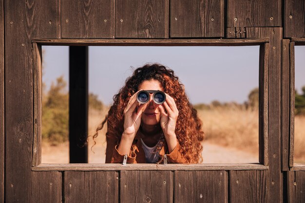 Femme rousse vue de face à la recherche à travers des jumelles