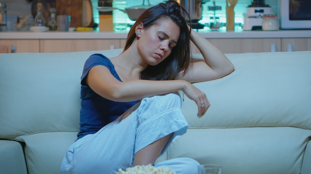 Femme s'endormant sur le canapé devant la télévision. Fatigué, épuisé, solitaire, endormi, en pyjama, dormant devant la télévision, assis sur un canapé confortable dans le salon, fermant les yeux en regardant un film la nuit