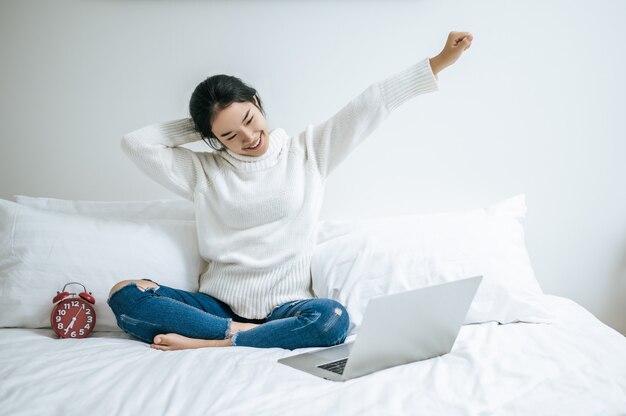 Cette femme s'est assise sur le lit, a levé la main et a posé l'ordinateur portable sur l'oreiller.