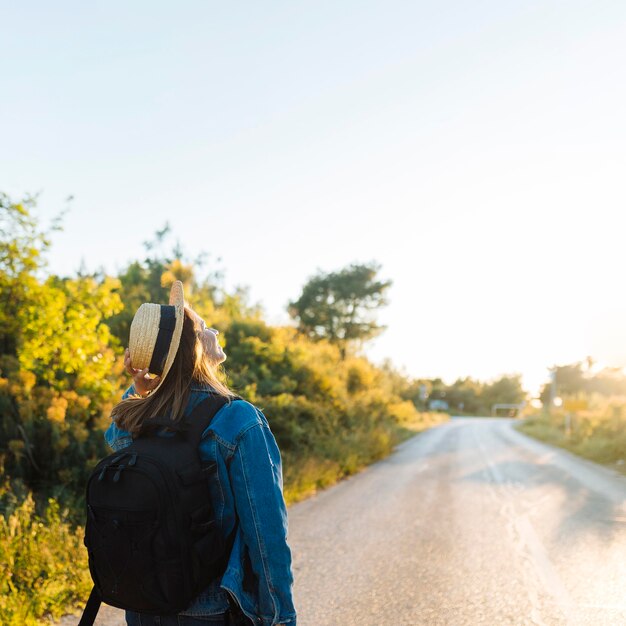 Une femme avec un sac à dos et un chapeau admirant la nature et le soleil