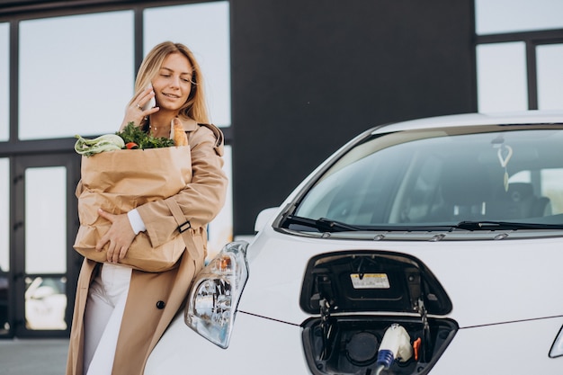 Femme avec des sacs de nourriture chargeant une voiture électrique