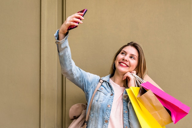 Femme avec des sacs à provisions prenant selfie au mur