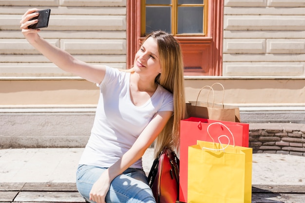 Femme avec des sacs à provisions prenant selfie avec smartphone