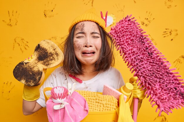 Une femme sale en détresse se sent surmenée après avoir passé toute la journée à nettoyer des poses avec une éponge et une éponge exprime des émotions négatives pose contre le mur jaune