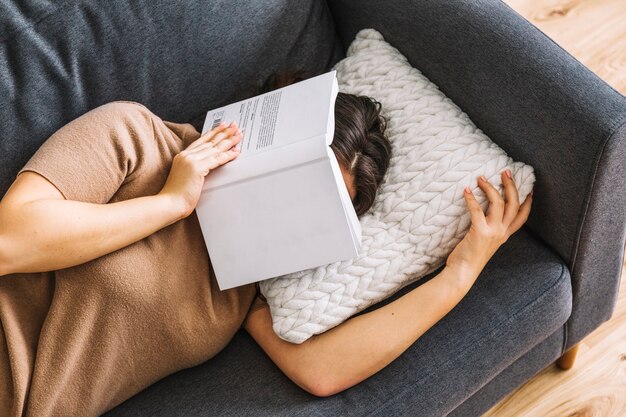 Femme sans visage avec livre de dormir sur le canapé