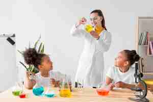 Photo gratuite femme scientifique enseignant la chimie des filles tout en tenant le tube avec potion