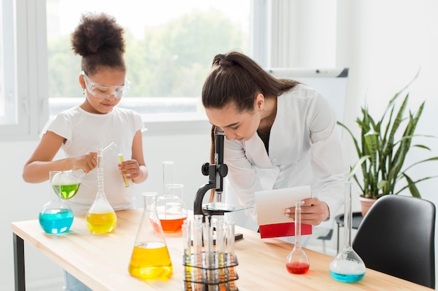 Femme scientifique regardant à travers le microscope avec une fille et des tubes à essai