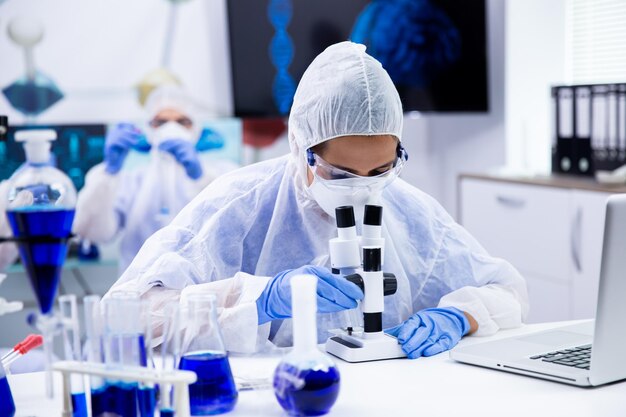 Femme scientifique regardant à travers un microscope en laboratoire de recherche. Fumer du liquide bleu dans des tubes à essai.