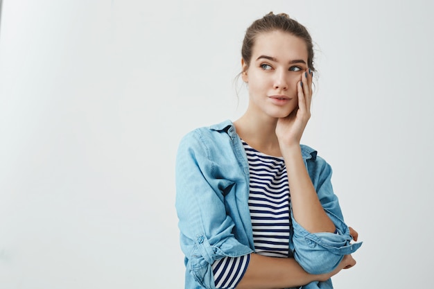 La femme se demande dans ses pensées. Portrait intérieur d'une charmante fille sensuelle avec une coiffure chignon tenant la paume sur la joue et regardant de côté l'espace de copie tout en rêvant ou en pensant à quelque chose