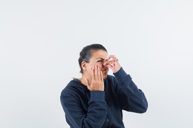 Femme se pinçant le nez dans un sweat à capuche et l'air dégoûté. vue de face.