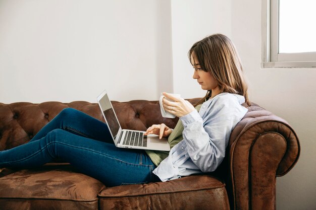 Femme se prélasser avec un café et un ordinateur portable