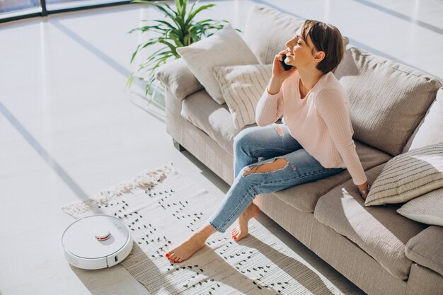 Femme se reposant sur un canapé pendant qu'un aspirateur robot fait le ménage