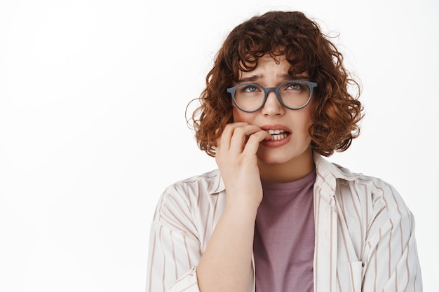 femme se rongeant les ongles et levant les yeux nerveux, se sentant inquiète en regardant en haut, paniquant, debout sur blanc