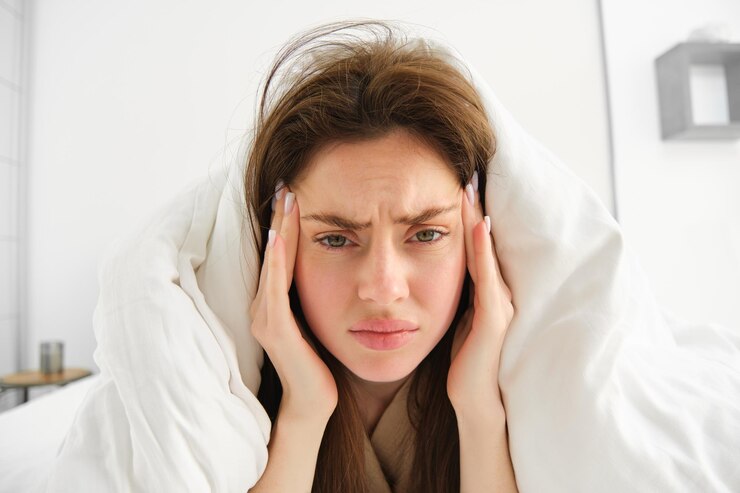 Photo gratuit femme se sentant mal au lit, allongée dans sa chambre sous une couverture et des draps blancs le matin, fronçant les sourcils