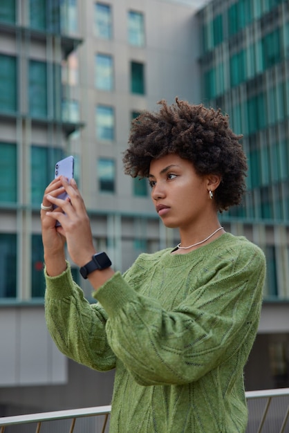 une femme se tient devant la caméra d'un téléphone portable, les prises de vue influencent le blog vidéo ou font des selfies utilisent des technologies modernes vêtues d'un pull vert décontracté