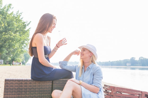 Femme, séance chaise lounge, regarder, elle, amis, tenue, bouteille eau, à, plage