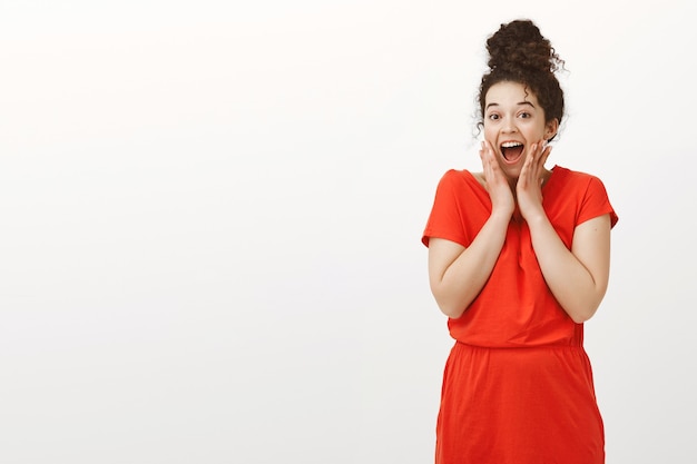 Femme séduisante excitée fascinée en robe rouge à la mode avec des cheveux en chignon, disant wow tout en étant étonné ou surpris