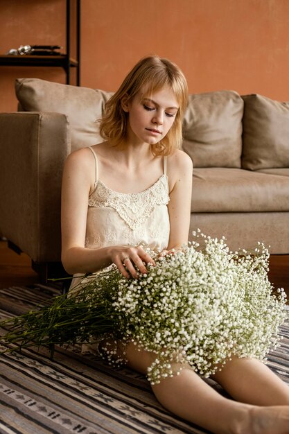 Femme séduisante posant à côté du canapé tout en tenant le bouquet de fleurs printanières délicates