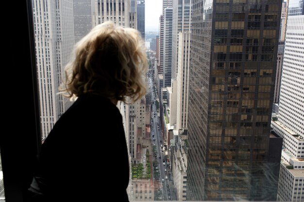 Une femme séduisante en robe de soie noire est assise sur un rebord de fenêtre en regardant New York