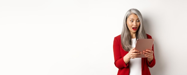 Femme senior asiatique d'affaires regardant l'écran de la tablette numérique avec une lecture de visage étonnée et surprise