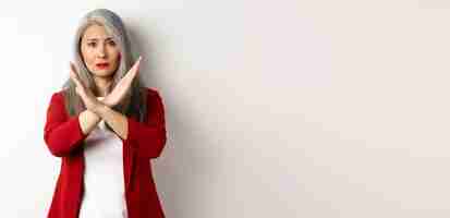 Photo gratuite femme senior asiatique en blazer rouge faisant un geste croisé vous suppliant d'arrêter de ne pas être d'accord et de désapprouver certains
