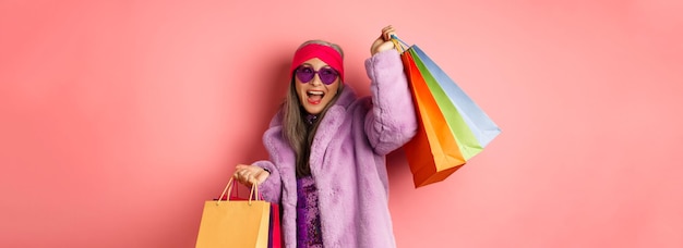 Photo gratuite femme senior asiatique élégante faisant du shopping portant des vêtements à la mode et des lunettes de soleil tenant des sacs de magasin a