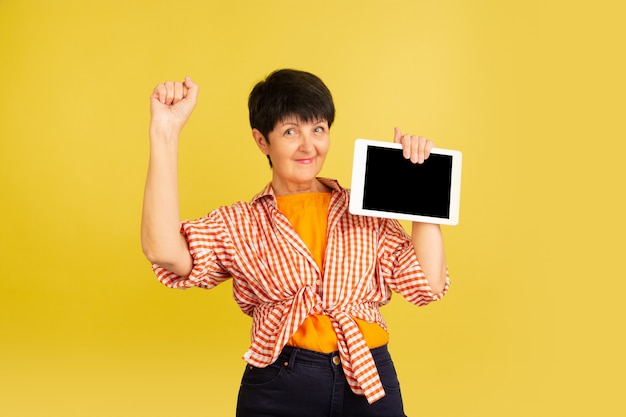 Femme senior isolée sur jaune. Concept de style de vie des personnes âgées tech et joyeux