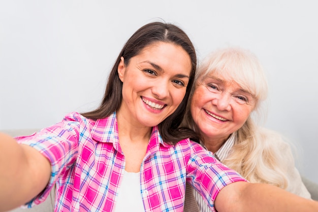 Femme senior joyeuse avec sa fille prenant autoportrait sur fond blanc