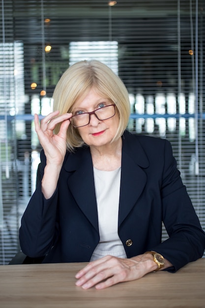 Une femme senior réussie ajustant les lunettes à la table