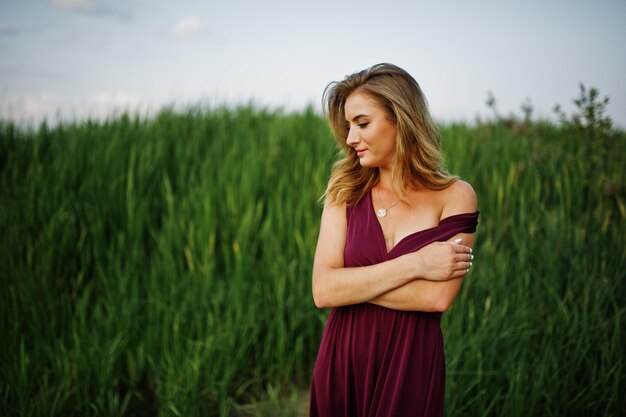 Femme sensuelle blonde en robe marsala rouge posant dans les roseaux