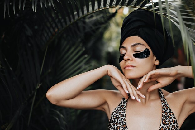 Femme sensuelle avec des cache-yeux debout sous le palmier. Belle femme en turban posant sur fond de nature.