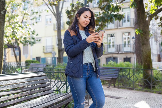 Femme sérieuse à l&#39;aide de smartphone et debout à l&#39;extérieur