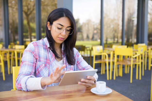 Femme sérieuse à l&#39;aide de tablette et de boire du café au café