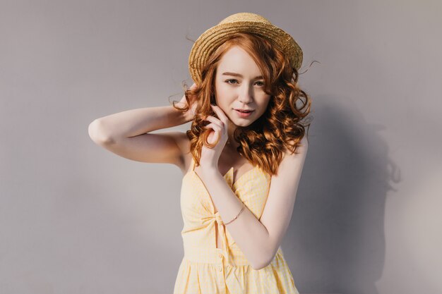 Femme sérieuse au gingembre en tenue d'été à la mode dansant sur un mur gris. Portrait d'une fille incroyable avec une coiffure ondulée posant en tenue jaune.