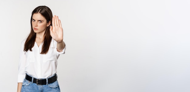 Photo gratuite femme sérieuse montrant un panneau d'arrêt en désaccord rejetant qch mauvais debout sur fond blanc