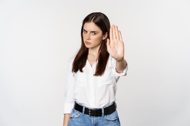 Femme sérieuse montrant un panneau d'arrêt, en désaccord, rejetant qch mauvais, debout sur fond blanc