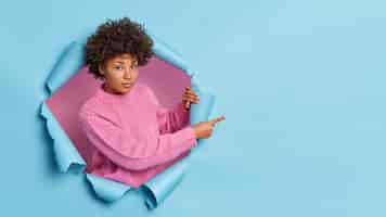 Photo gratuite une femme sérieuse à la peau foncée et aux cheveux bouclés a un regard confiant vous recommande quelque chose