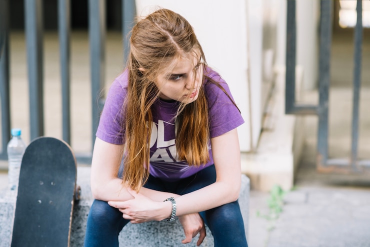 Photo gratuit femme sérieuse s&#39;assoit avec son skateboard regardant vers la gauche