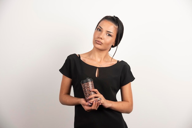 Femme sérieuse avec une tasse de café posant sur un mur blanc.