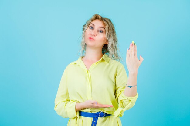 Une femme sérieusement blonde montre sa main à la caméra sur fond bleu