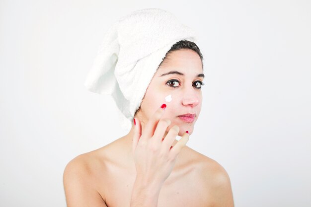 Femme avec une serviette blanche enroulée autour de sa tête, appliquant de la crème sur le visage