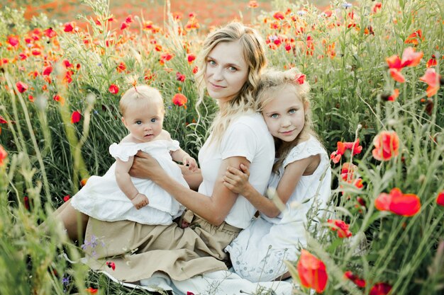 Femme avec ses deux filles s'accroupit dans un champ de coquelicot
