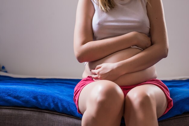 Femme avec ses douleurs menstruelles mensuelles agrippant son estomac avec ses mains alors qu&#39;elle est stressée par les crampes en cours, la vue du torse de ses mains et son ventre