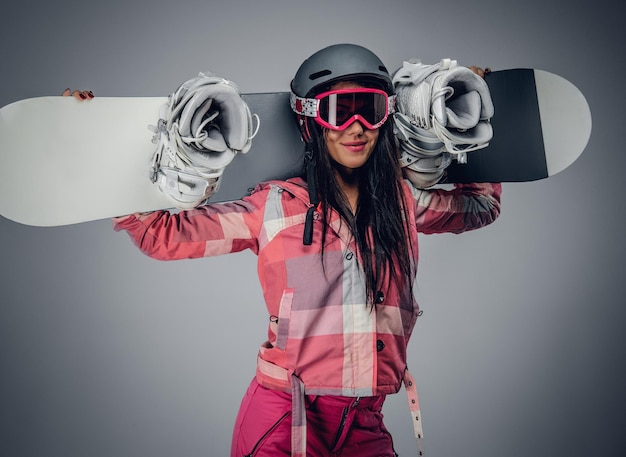 Femme sexy en costume de ski posant avec snowboard dans un studio sur fond gris.