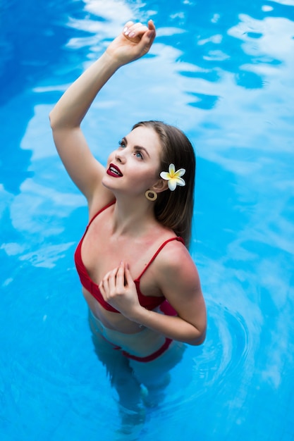 Femme sexy élégante en bikini rouge sur le corps mince et galbé bronzé au soleil nager dans la piscine