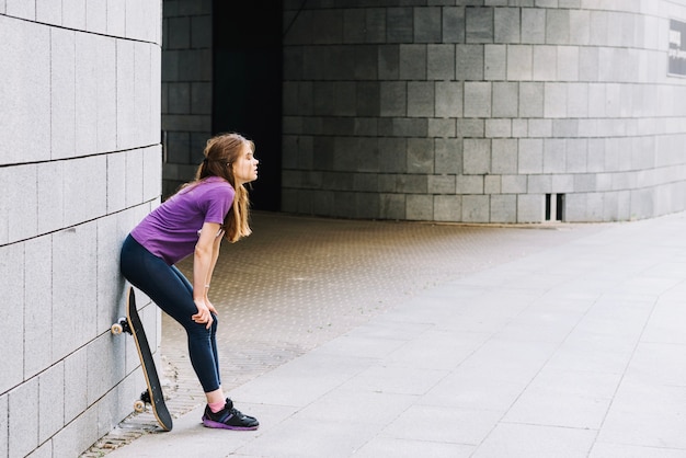 Femme skateboarder repose contre le mur de briques