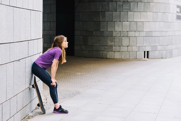 Femme skateboarder repose contre le mur de briques