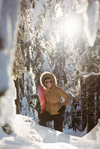 Femme avec snowboard marchant sur la montagne enneigée