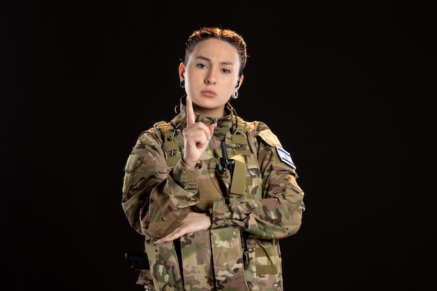 Une femme soldat en camouflage met en garde sur un mur noir